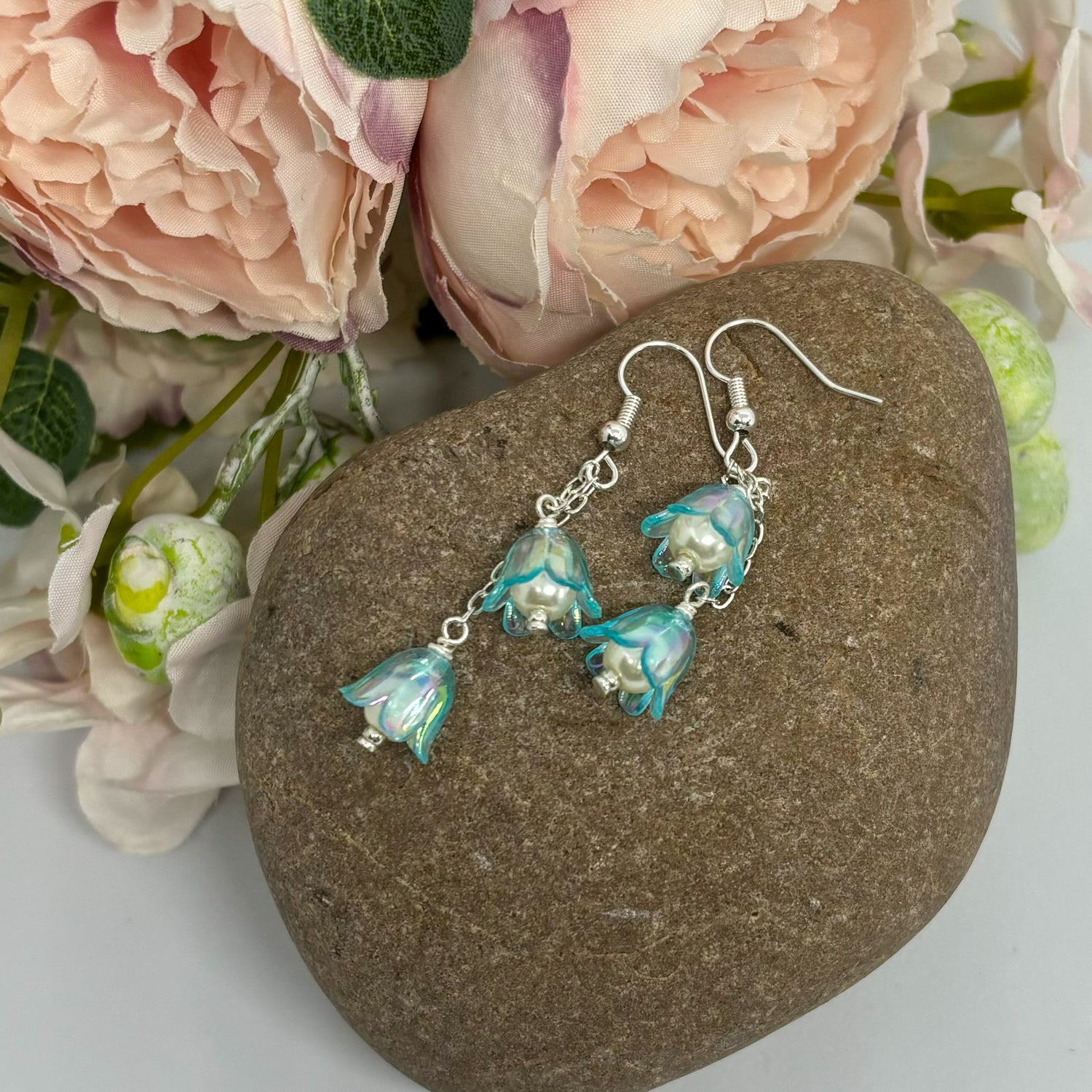 blue tulip earrings on a stone with flowers behind.