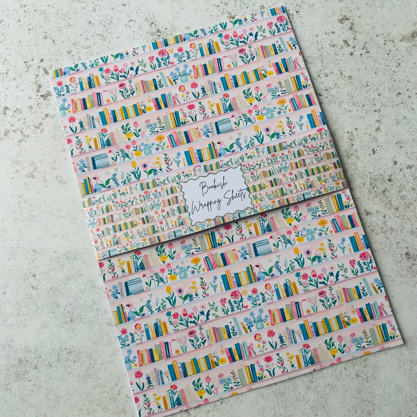 Two sheets of decorative paper with floral and book design on a concrete surface