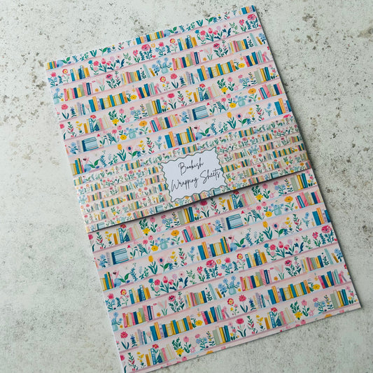 Two sheets of decorative paper with floral and book design on a concrete surface