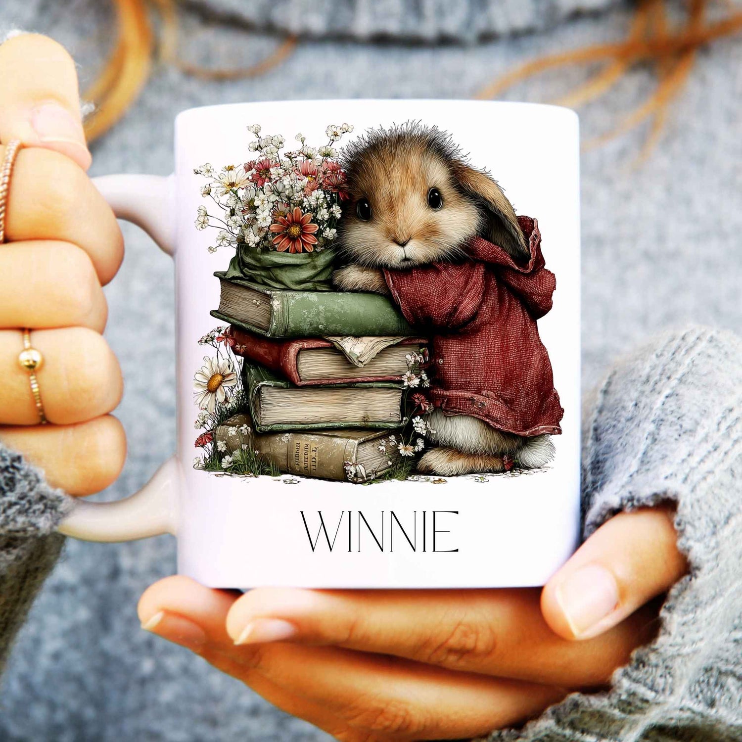 Mug with a rabbit illustration and 'Winnie' text held by hands.