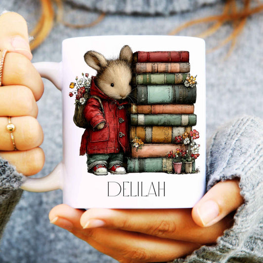 Mug with a mouse character in a red coat and books, held by hands.