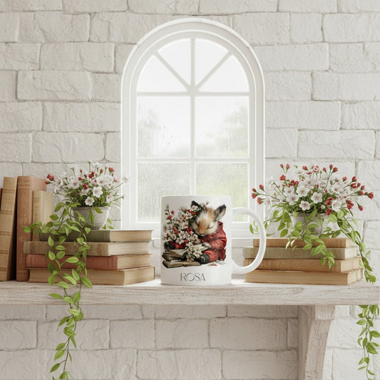 White mug with a mouse design on a table with books and flowers, against a stone wall.