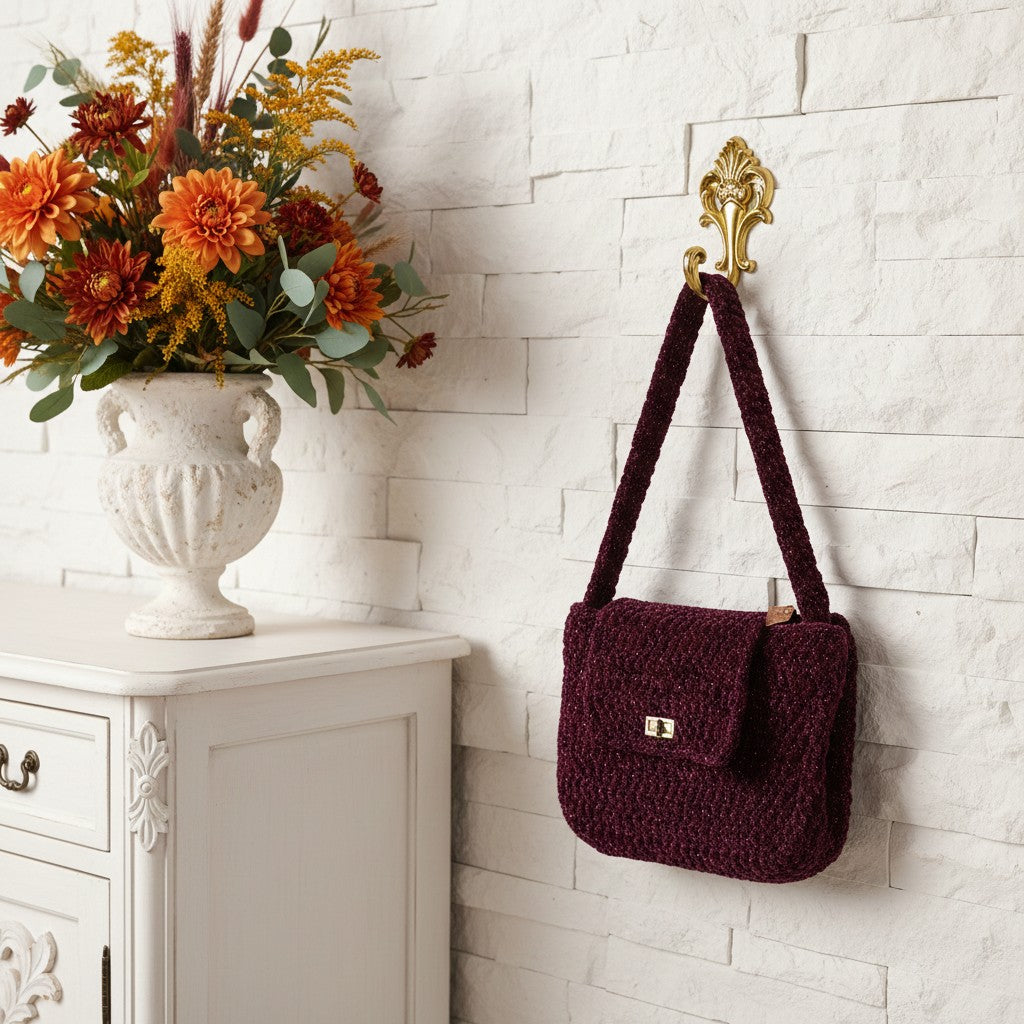 burgundy crochet bag hung on a hook and next to a vase full of autumnal flowers