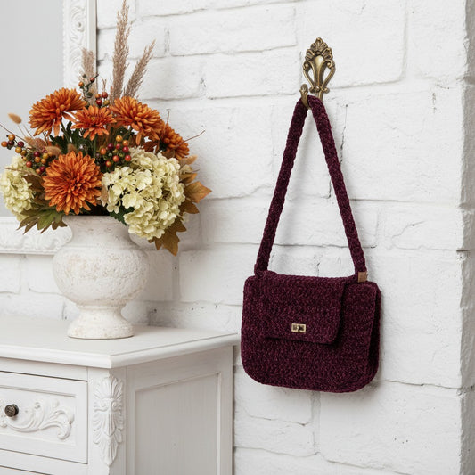 Pretty crochet handbag in burgundy hung on a hook next to a sideboard with flowers in a vase