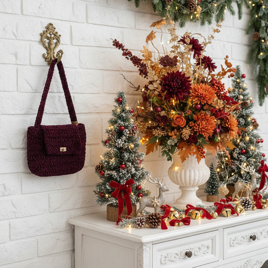 Decorative setup with a handbag, Christmas trees, and floral arrangement on a white surface.