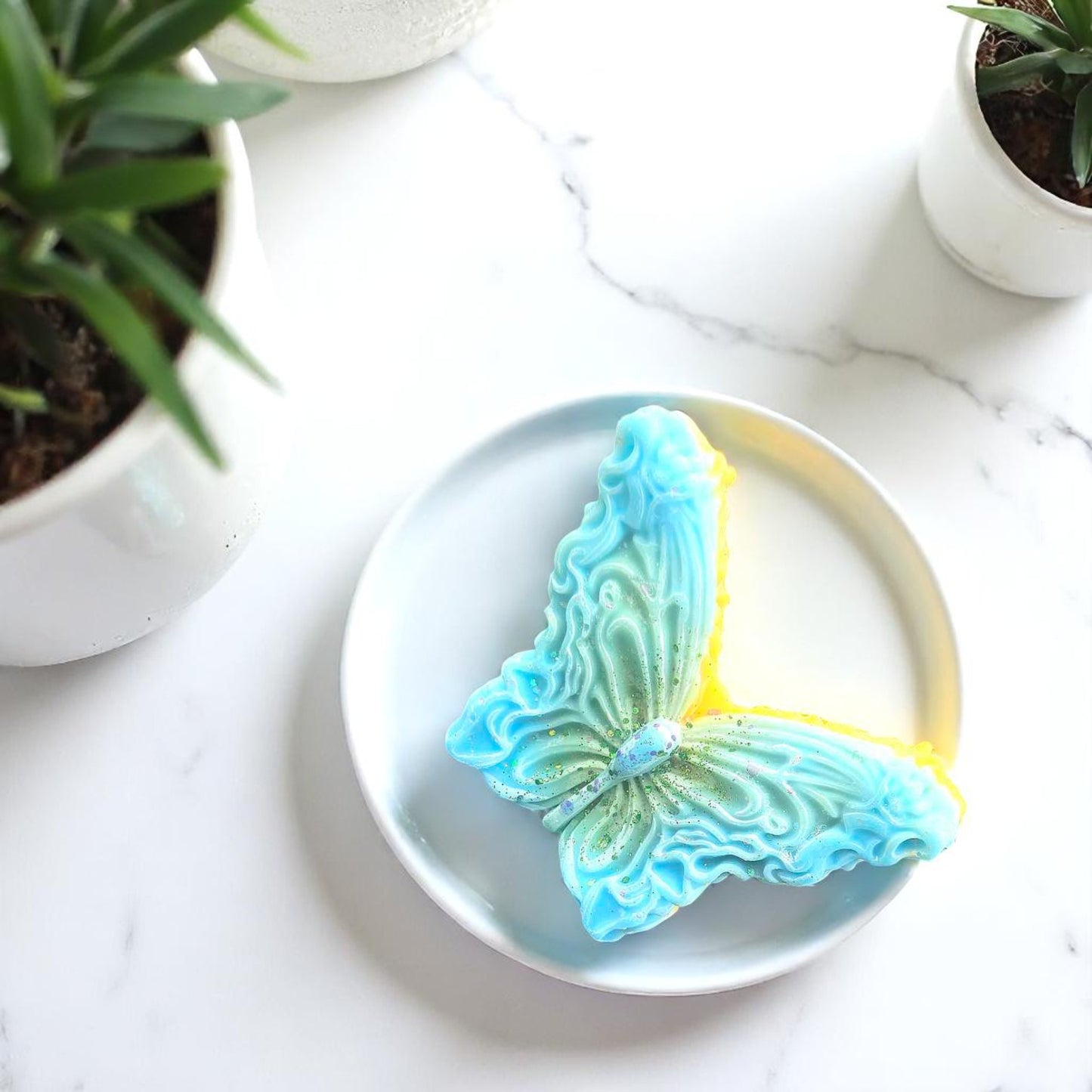 Butterfly-shaped wax melts on a white plate with plants in the background