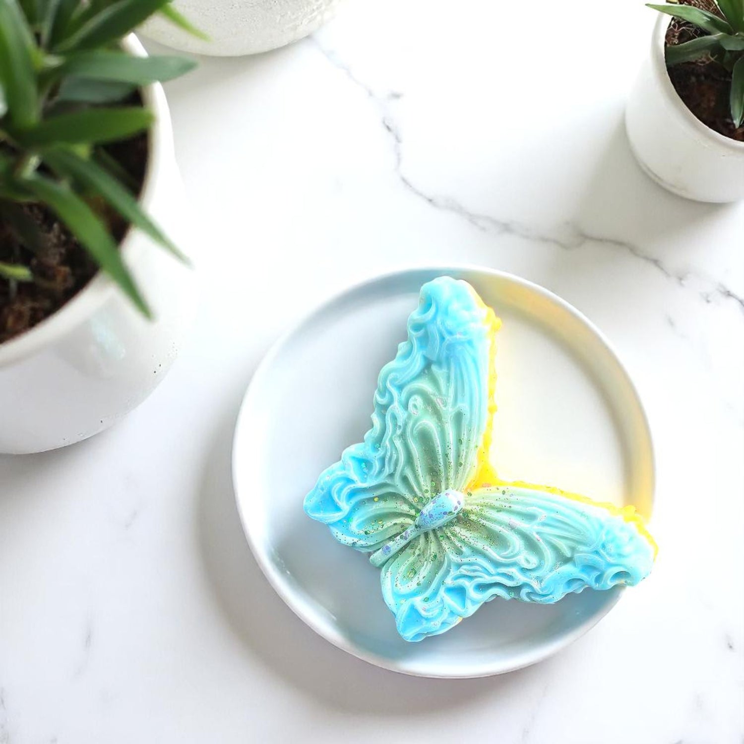 Butterfly-shaped wax melts on a white plate with plants in the background