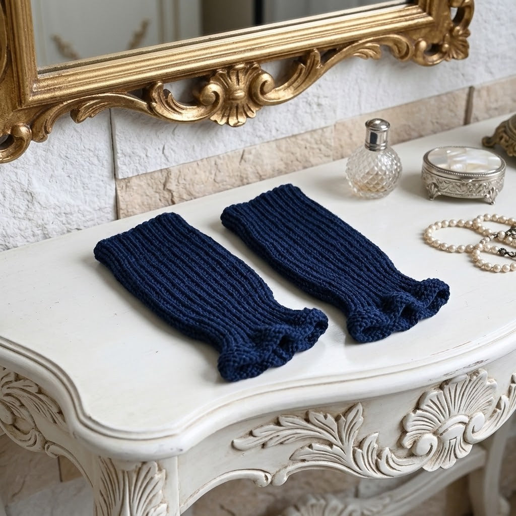 A pair of navy blue ribbed fingerless gloves displayed on an ornate white console table with a gold mirror, decorative perfume bottle, and pearl necklace nearby.