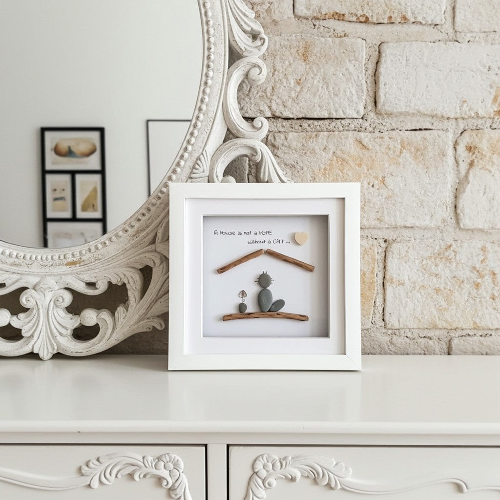 A white square shadow box frame containing an owner and a cat made from pebbles with a lovely quote