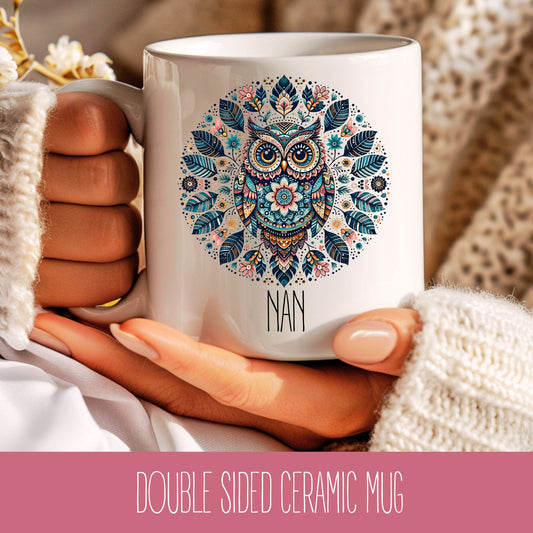 A ceramic coffee mug with a colourful owl design in the centre, held in a person's hand, with a sweater-clad arm in the background.