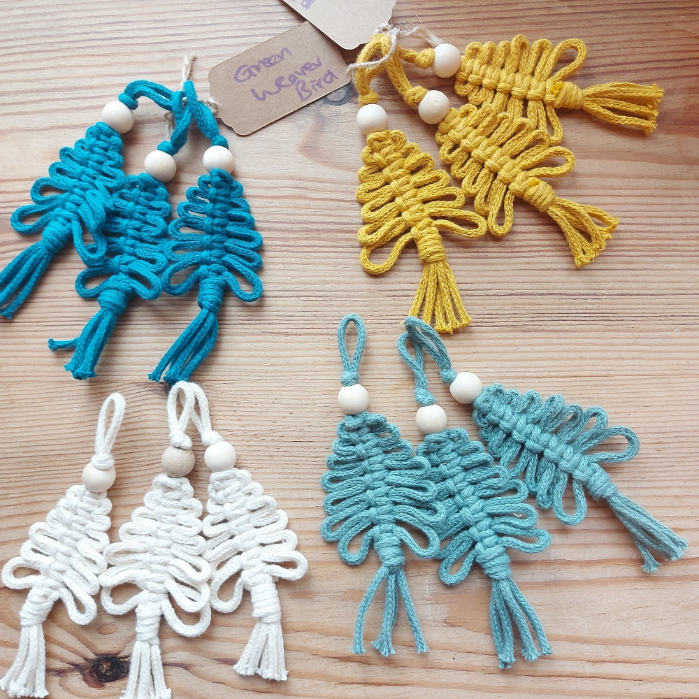 A selection of handmade macrame Christmas decorations in various colours, including blue, green, yellow, and white, each featuring a unique weave design.