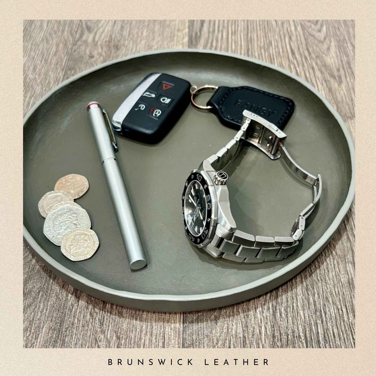 Silver watch, pen, car keys, and coins on a grey leather tray with 'Brunswick Leather' branding.