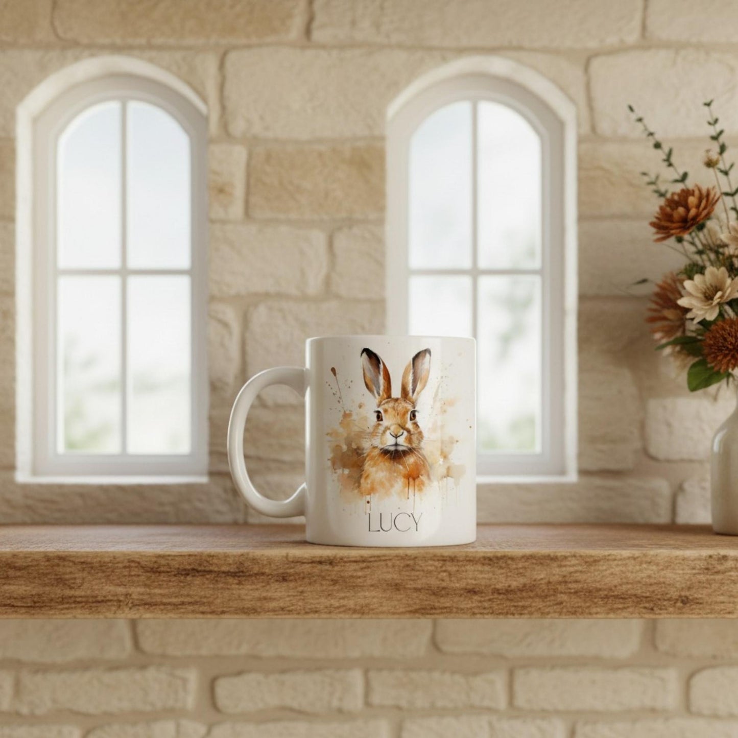 White mug with a hare design and 'LUCY' text on a wooden shelf with a stone wall background.