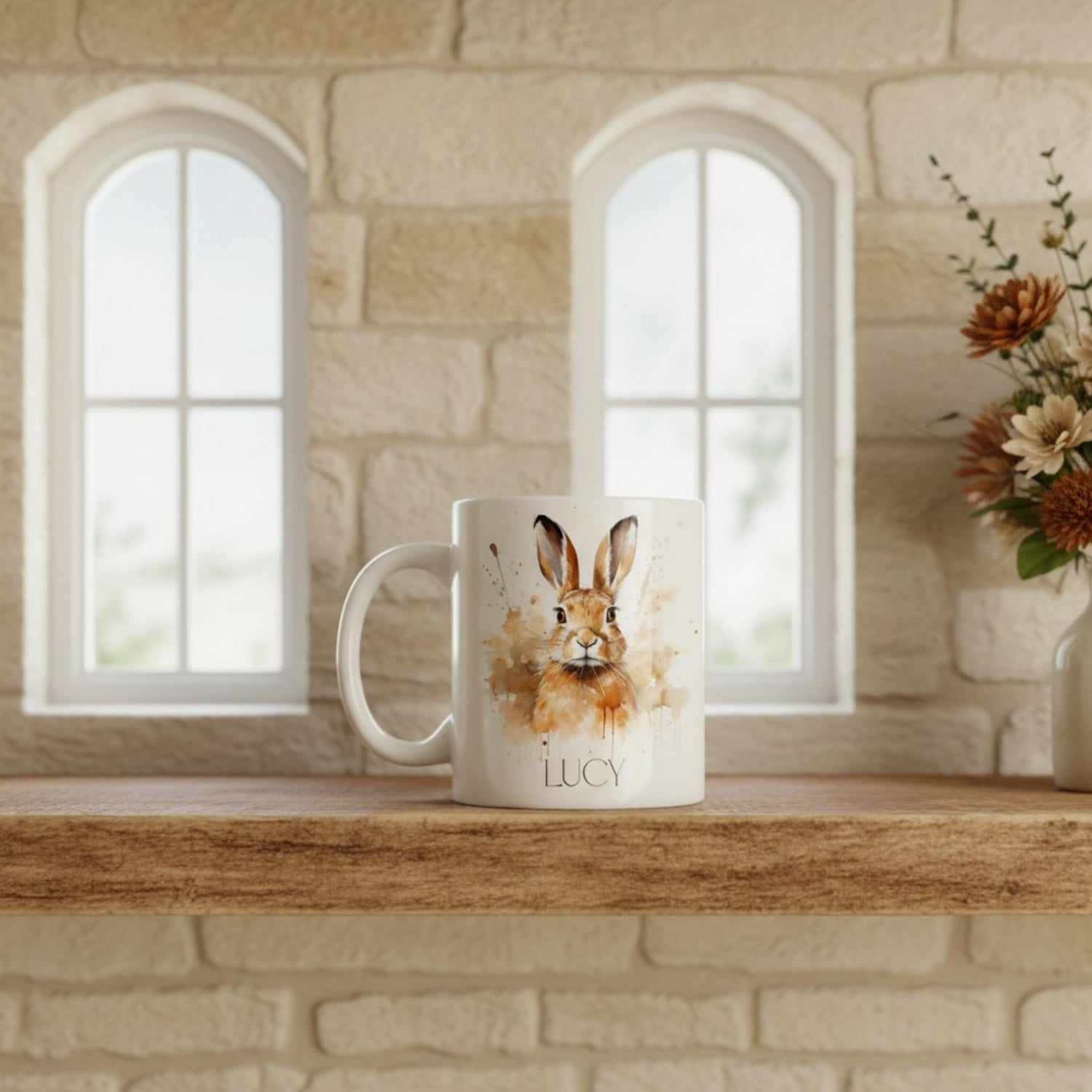 White mug with a hare design and 'LUCY' text on a wooden shelf with a stone wall background.