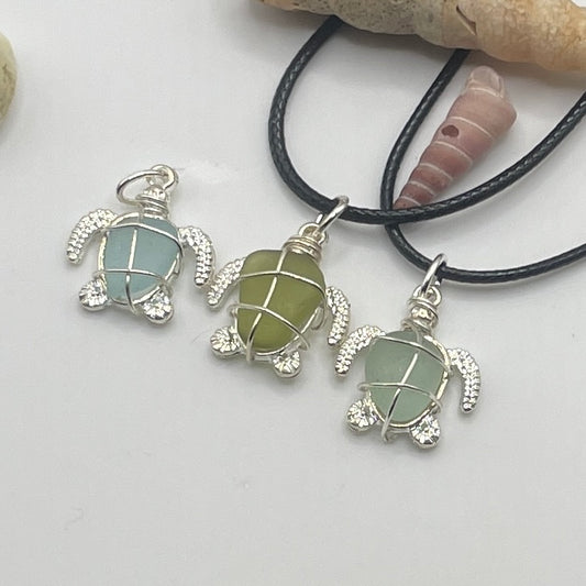 Three cornish sea glass turtle necklaces with a shell behind.