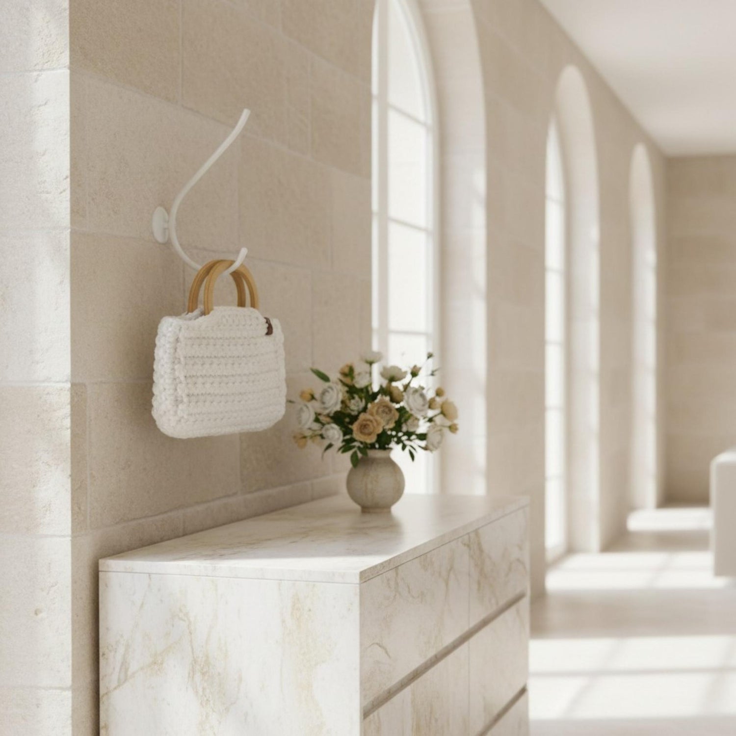 White crochet bag with wooden handle hung on a hook next to flowers on a sideboard.