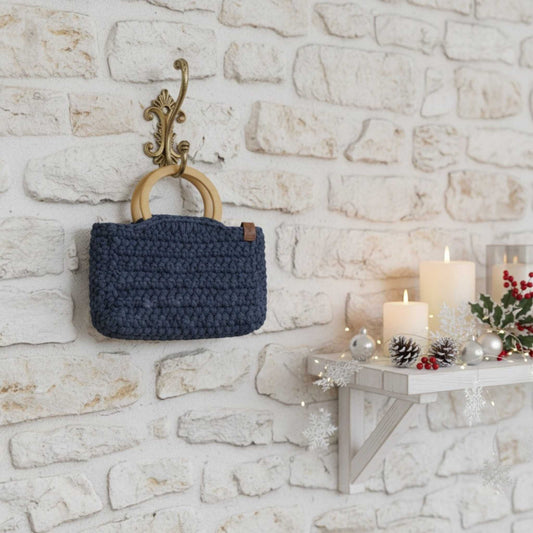 Blue woven bag hanging on a decorative wall hook against a stone wall with candles and decorations.