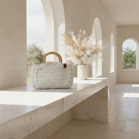 White crochet bag on a sideboard with flowers next to it.