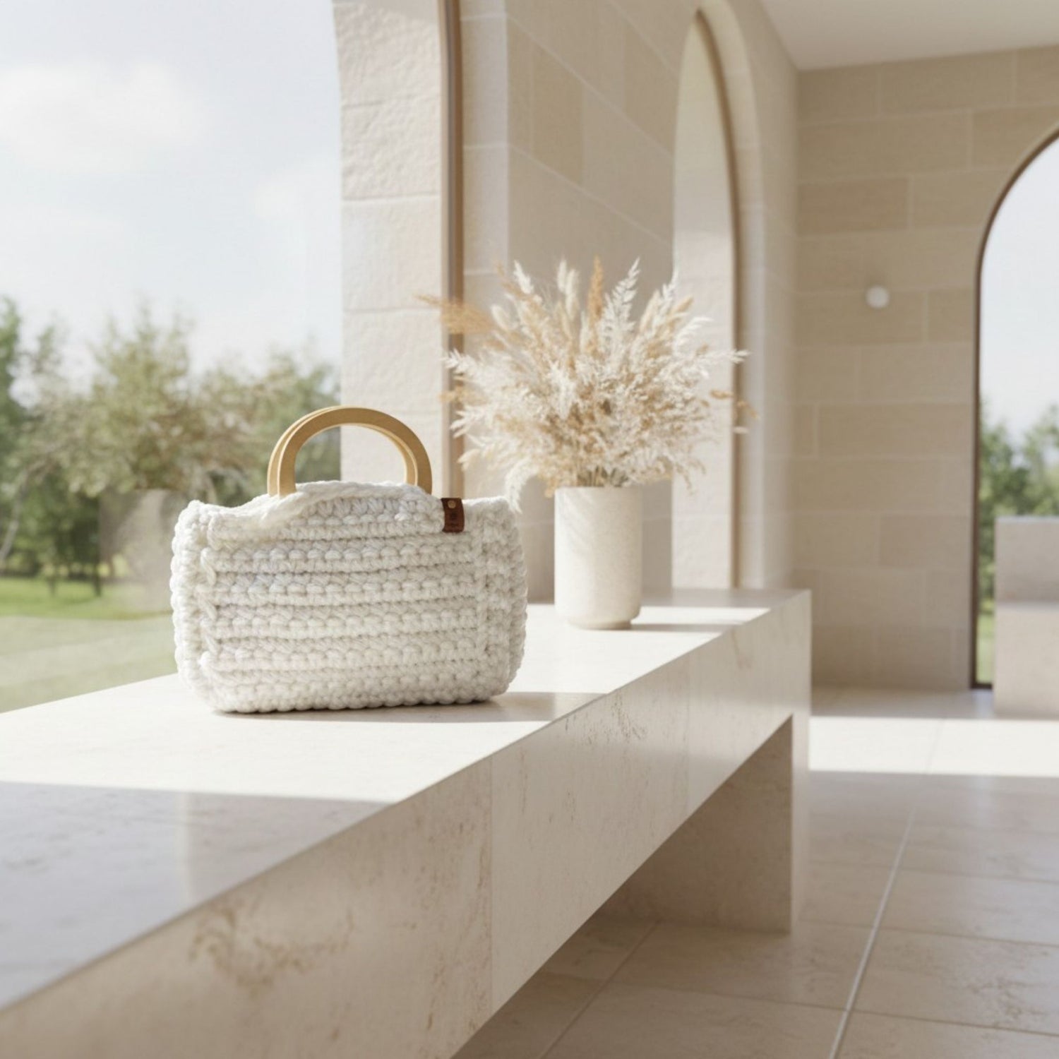 Handmade white crochet bag on a sideboard with dried flowers in a vase.