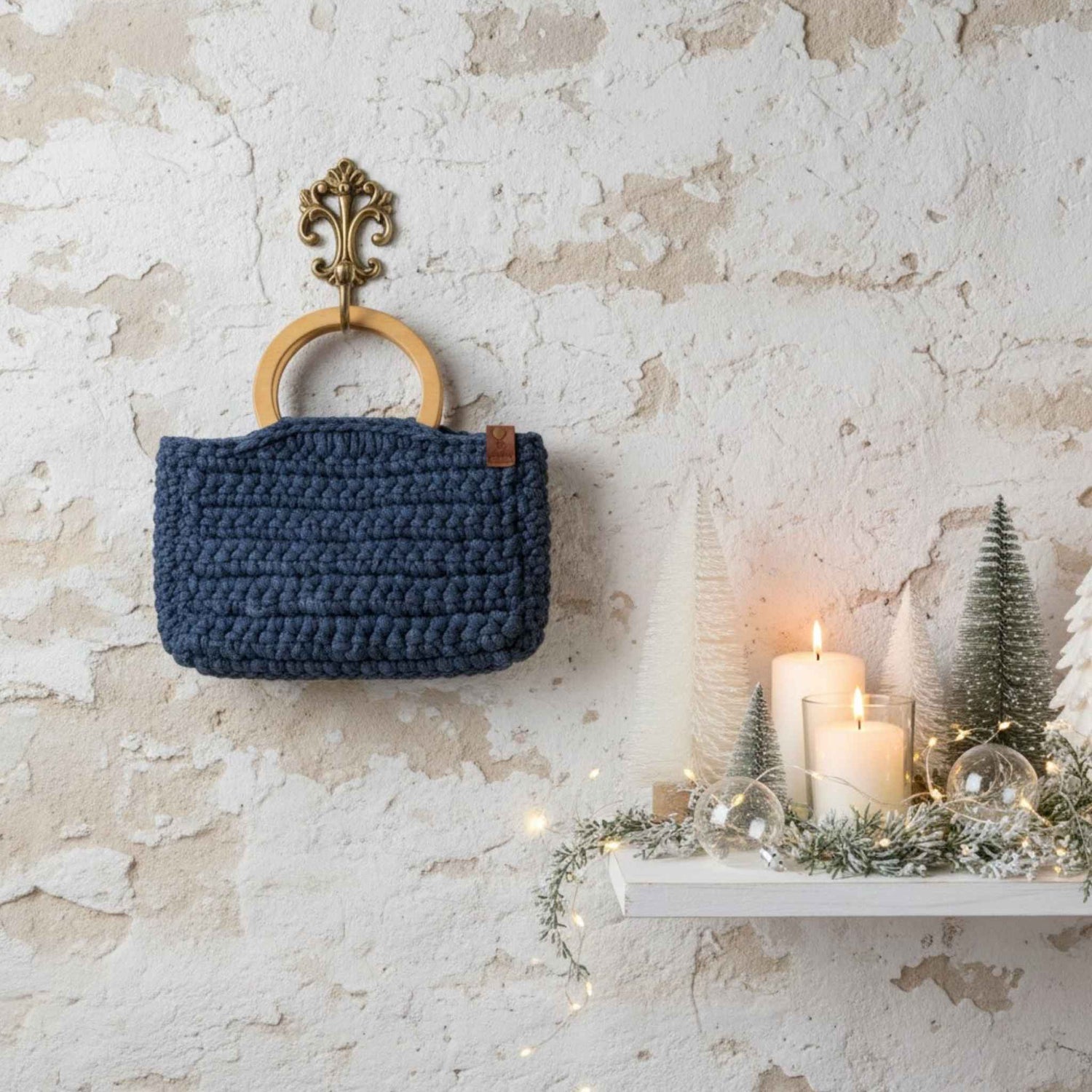 Blue woven bag with wooden handle hanging on a textured wall with candles and decorative trees.
