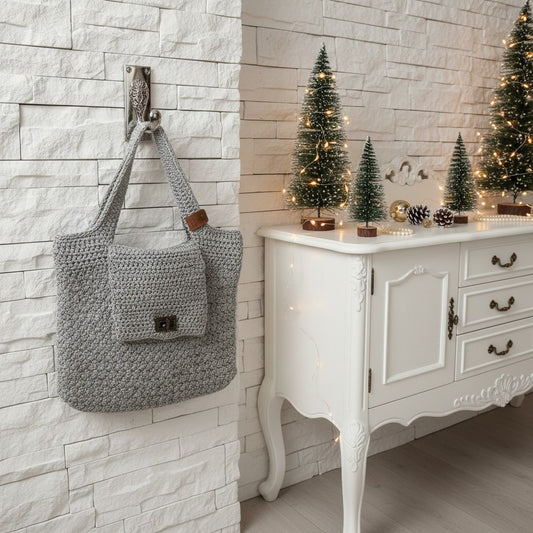 Grey crochet bag hanging on a wall hook next to a white dresser with decorative Christmas trees.