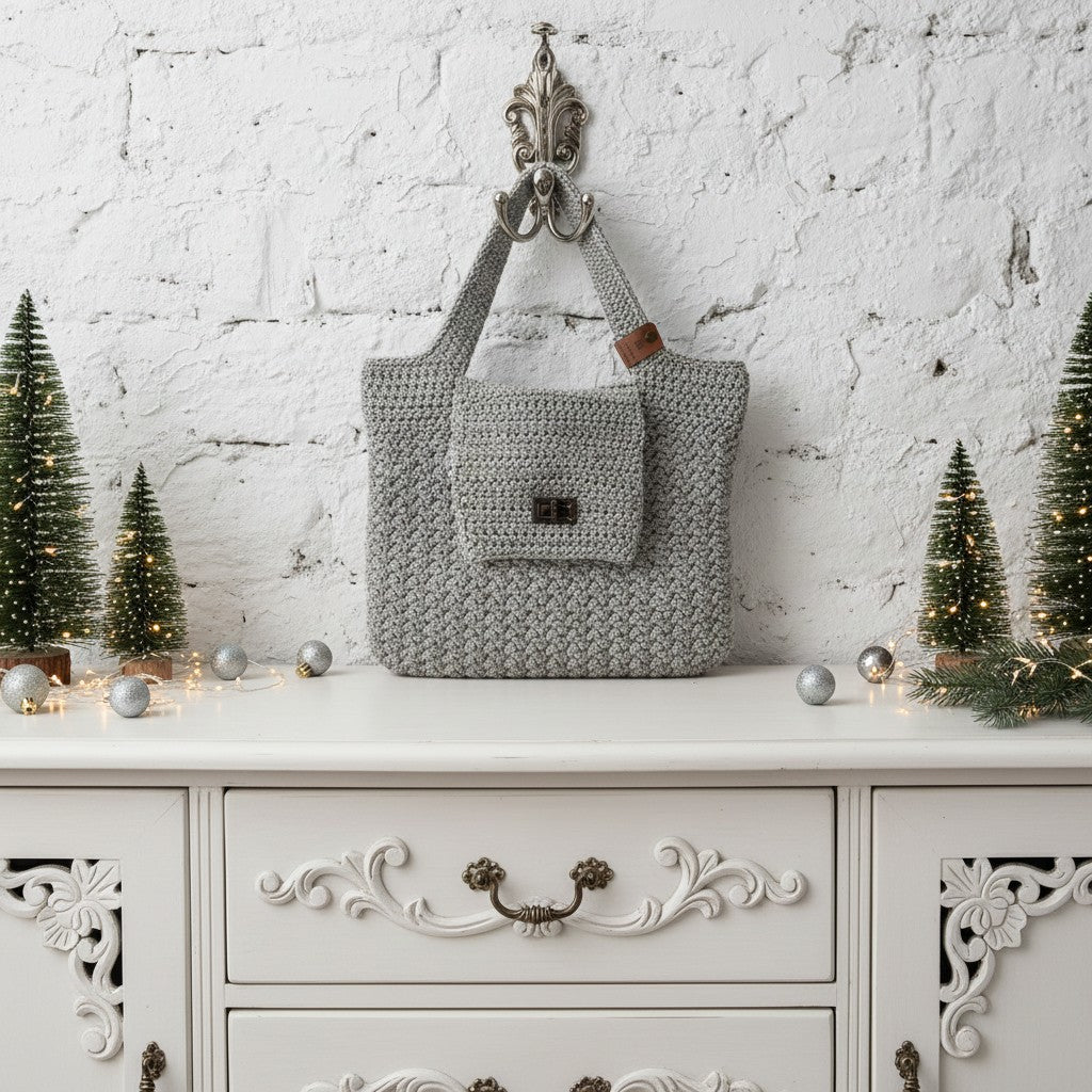 Grey knitted bag hanging on a decorative hook with Christmas trees and lights in the background.