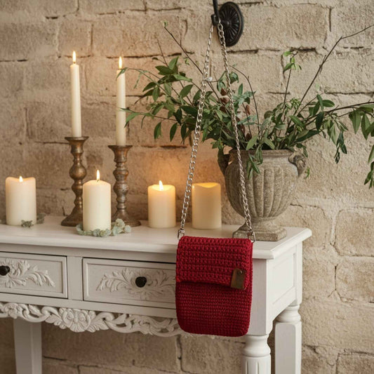 Red woven phone bag on a white table with candles and a plant against a stone wall.