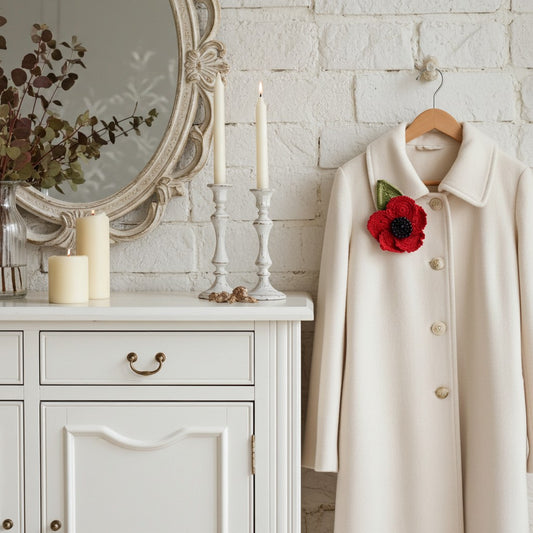 Beige coat with a red remembrance poppy brooch on a hanger next to a white cabinet with candles and a mirror.