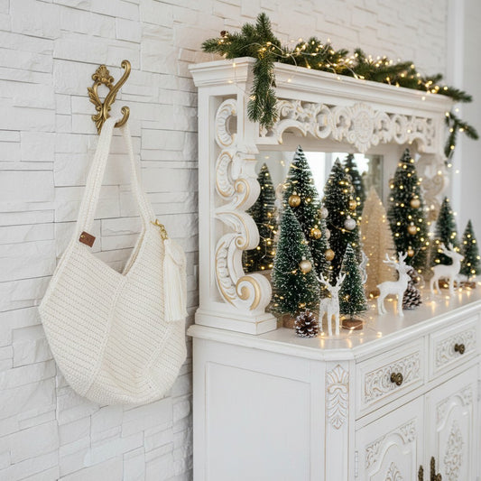 Crochet shopper bag with decorative Christmas mantel with small trees, lights, and deer figurines on a white wall.