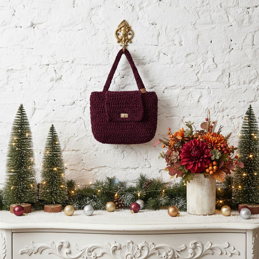 Maroon handbag hanging on a decorative wall with Christmas decorations and flowers.