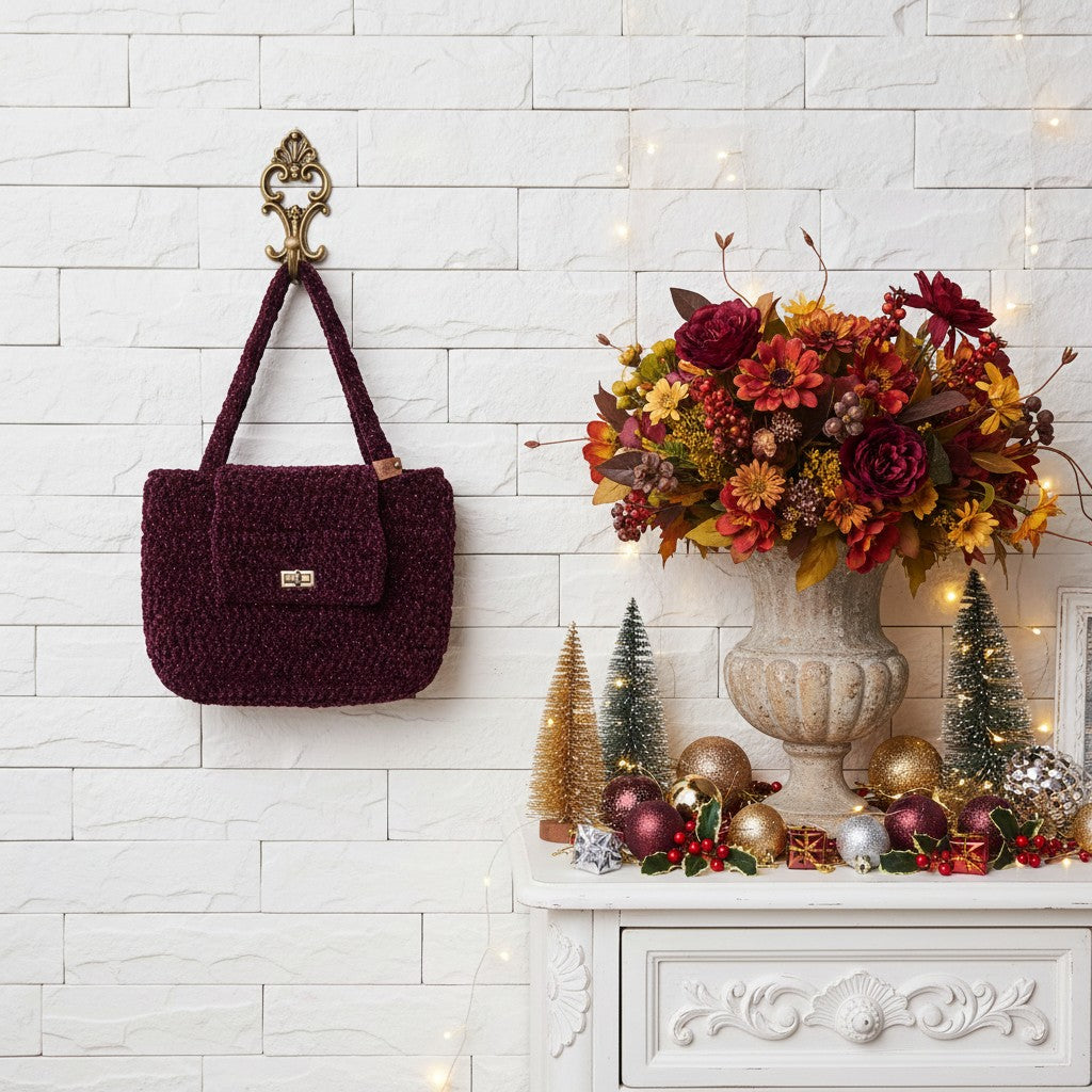 Decorative scene with a maroon handbag, floral arrangement, and festive decorations on a white brick wall.