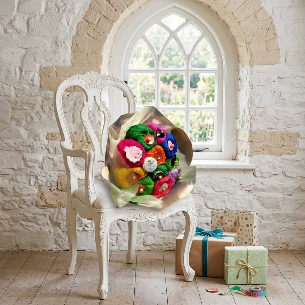 A colourful bouquet of knitting yarn, displayed on an ornate white armchair in a bright room with a stone wall and arched window. Two wrapped gift boxes sit on the floor nearby.