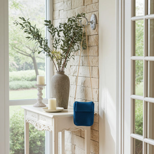 Decorative setup with a vase, candles, and a turquoise phone bag on a white table by a window.