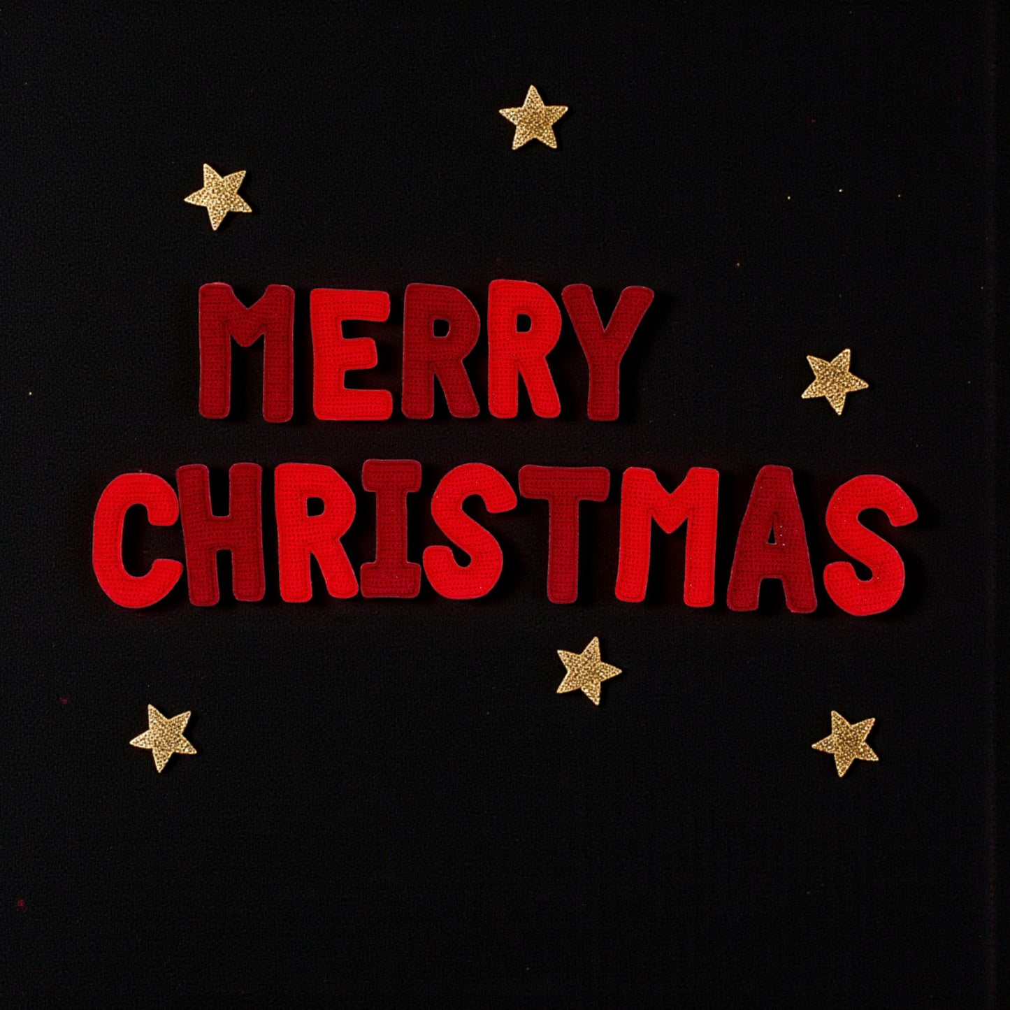 crochet letters saying  'merry christmas'  with gold stars on a black background