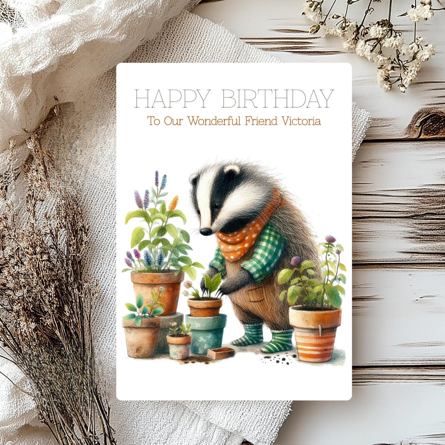Birthday card with a badger character gardening, surrounded by plants and flowers on a rustic wooden surface.