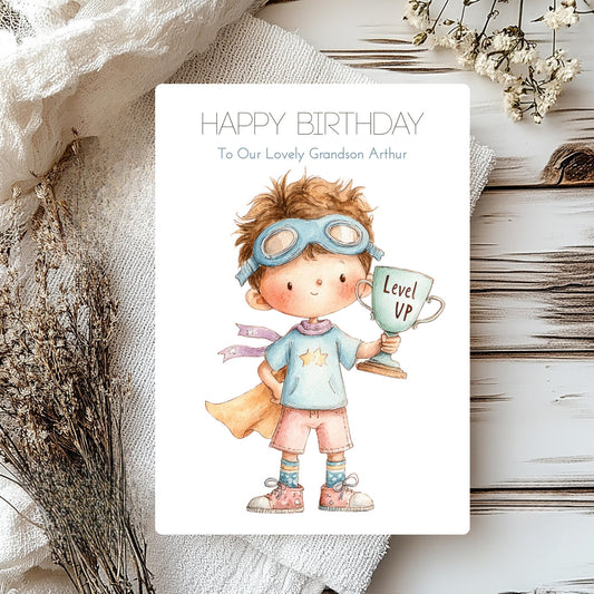 Birthday card with a child holding a 'Level Up' cup on a textured surface with flowers.