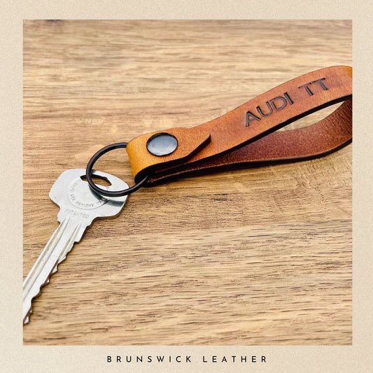 Leather keychain with 'Audi' branding on a wooden surface, featuring the brand 'Brunswick Leather'.