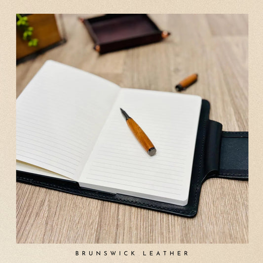 Open notebook with a pen on a wooden surface, featuring Brunswick Leather branding.