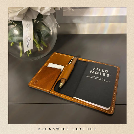 Field Notes notebook with pen holder and pen on a table with flowers in the background