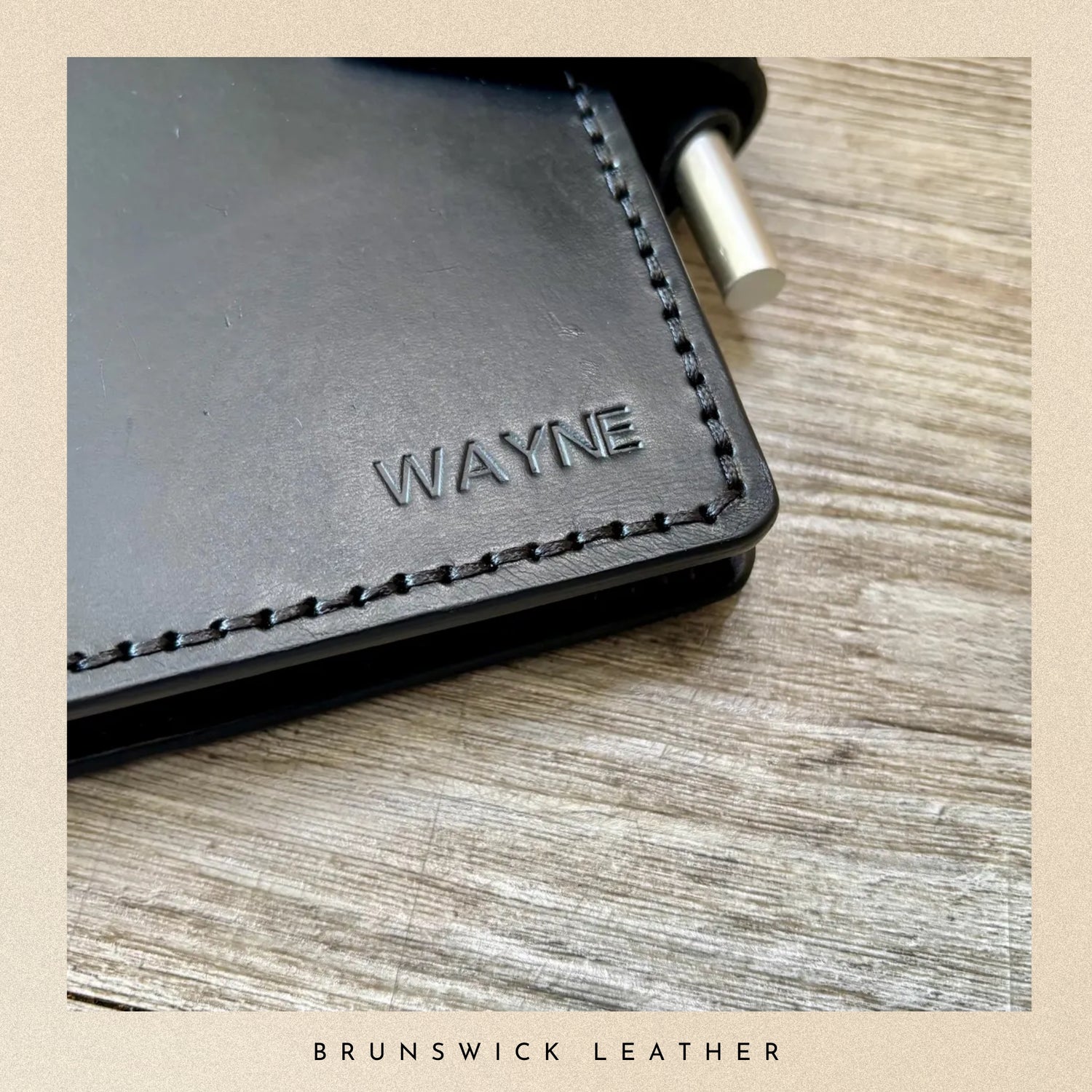 Black leather wallet with 'WAYNE' branding on a wooden surface, featuring Brunswick Leather.