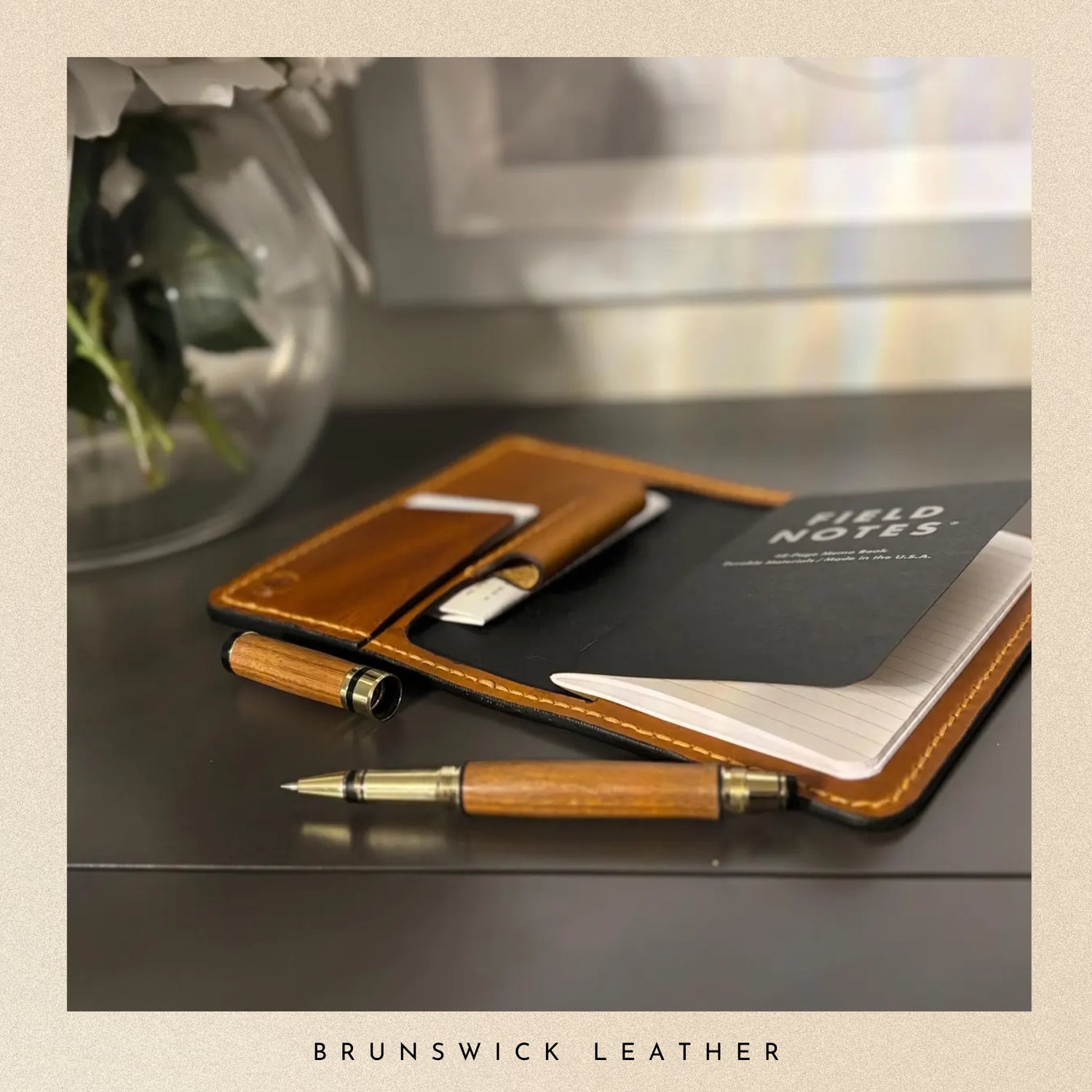 Wooden pen and leather wallet on a reflective surface with 'Field Notes' notebook.