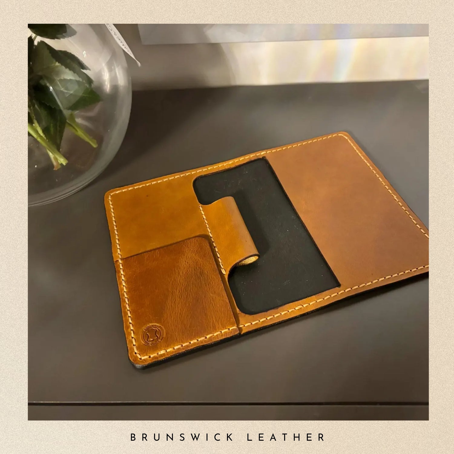 Brown leather phone case on a gray surface with 'Brunswick Leather' branding.