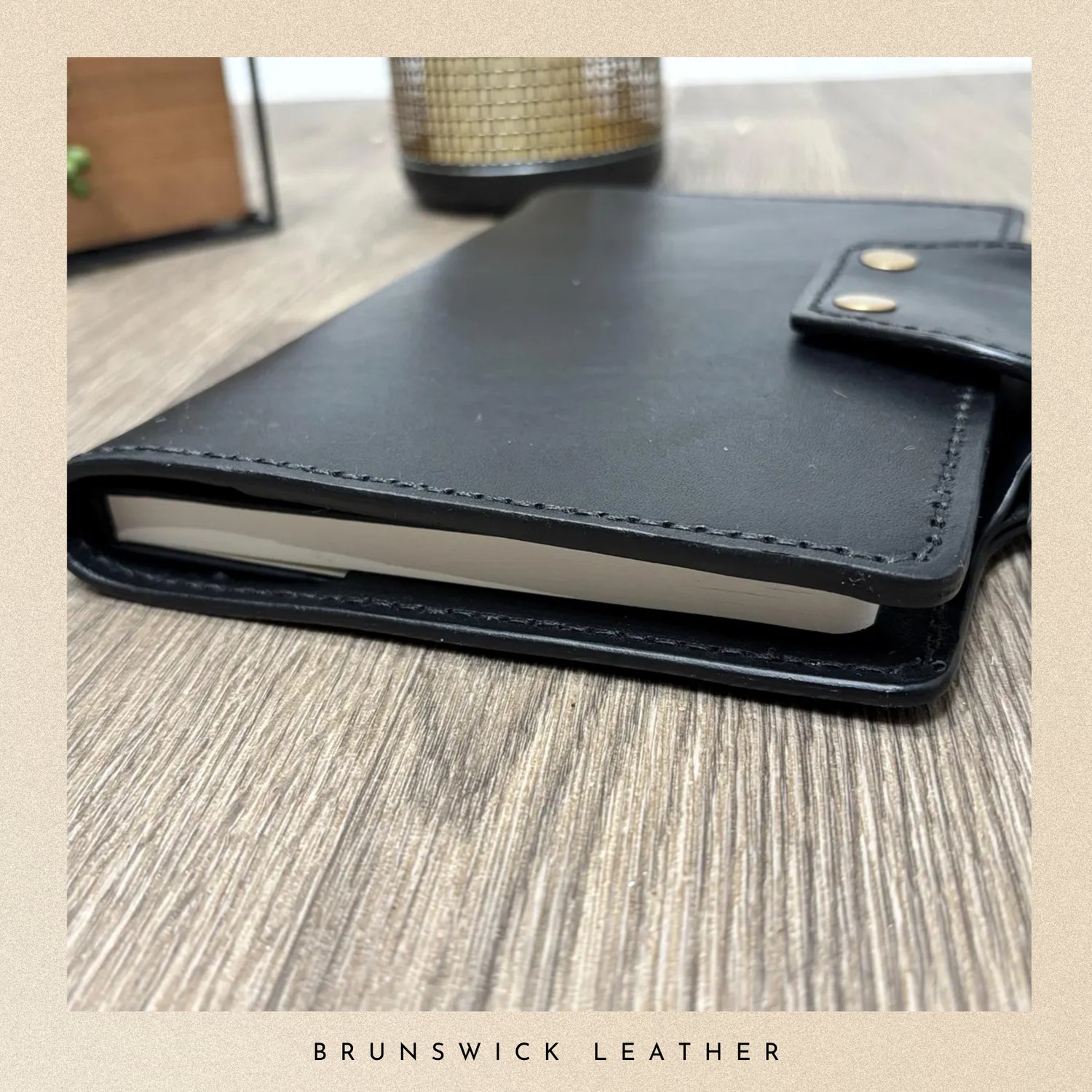 Black leather notebook on a wooden surface with 'Brunswick Leather' branding.