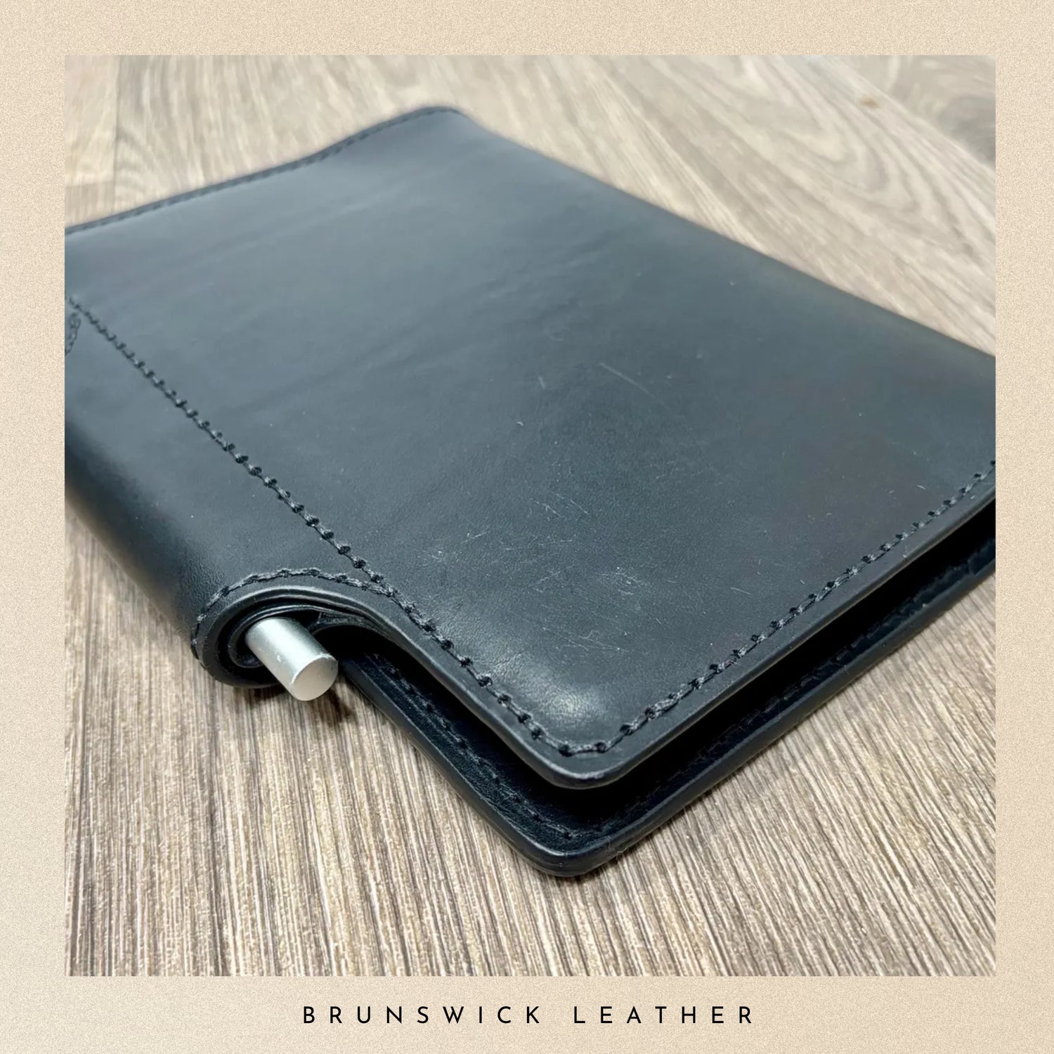 Black leather wallet with a metallic clip on a wooden surface, branded 'Brunswick Leather'.