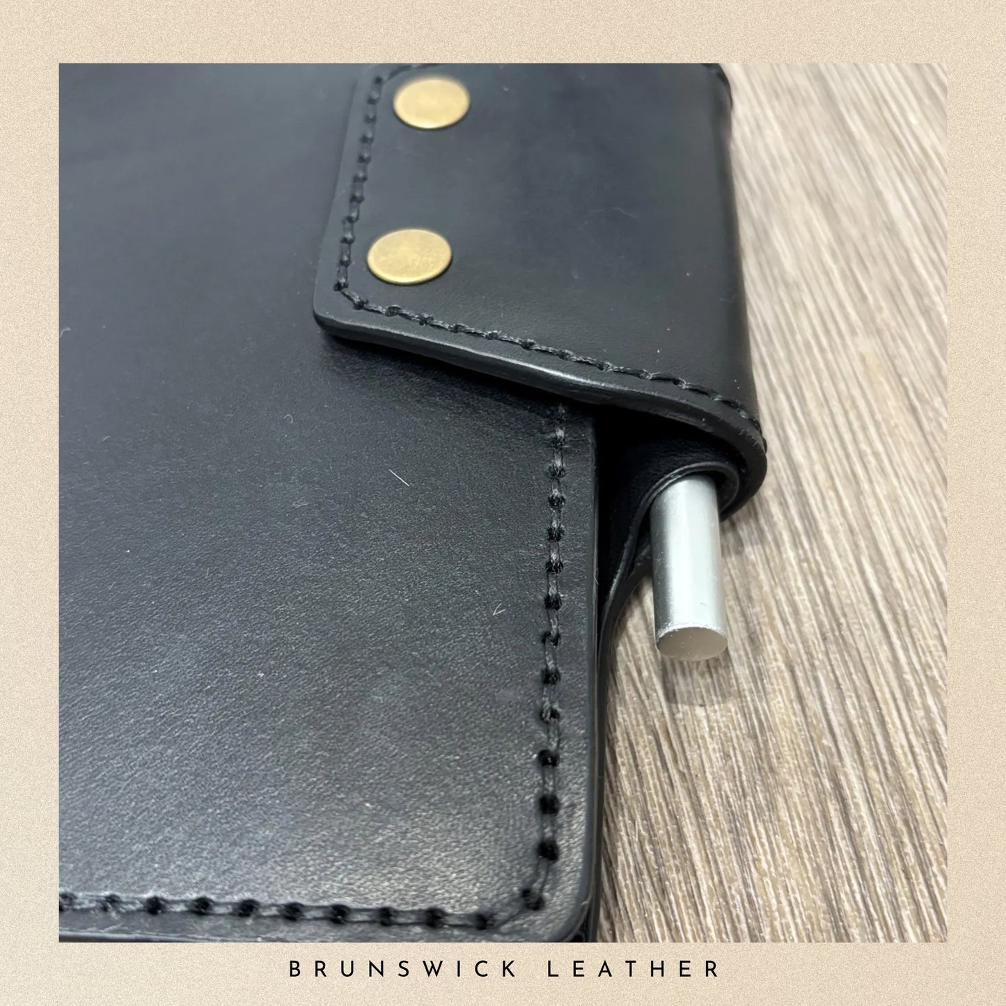 Black leather pen holder with gold studs on a wooden surface, featuring 'Brunswick Leather' branding.