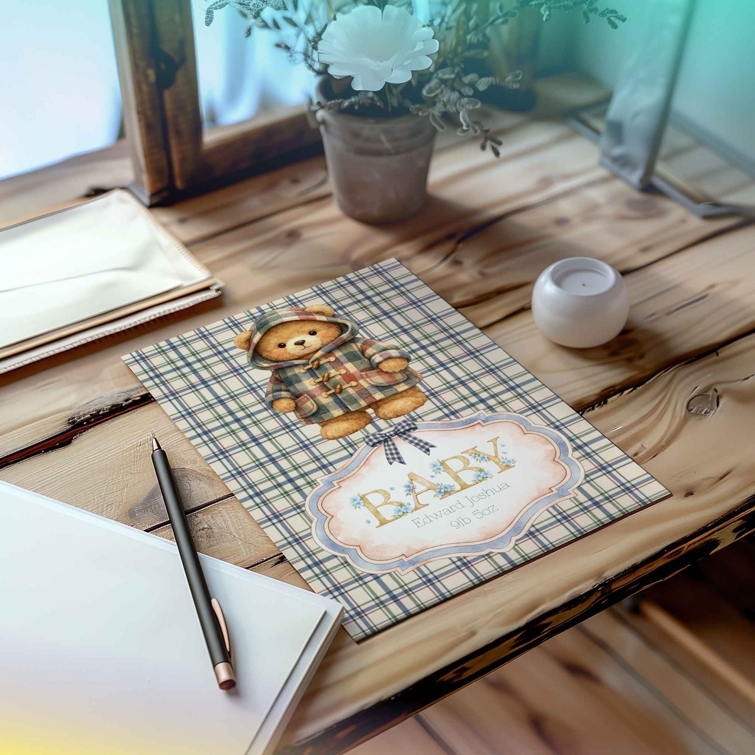 A baby shower card featuring a teddy bear in a plaid outfit and a decorative label that reads 'BABY' with baby weight and name, displayed on a rustic wooden table with a candle, notebook, and flowers in the background.