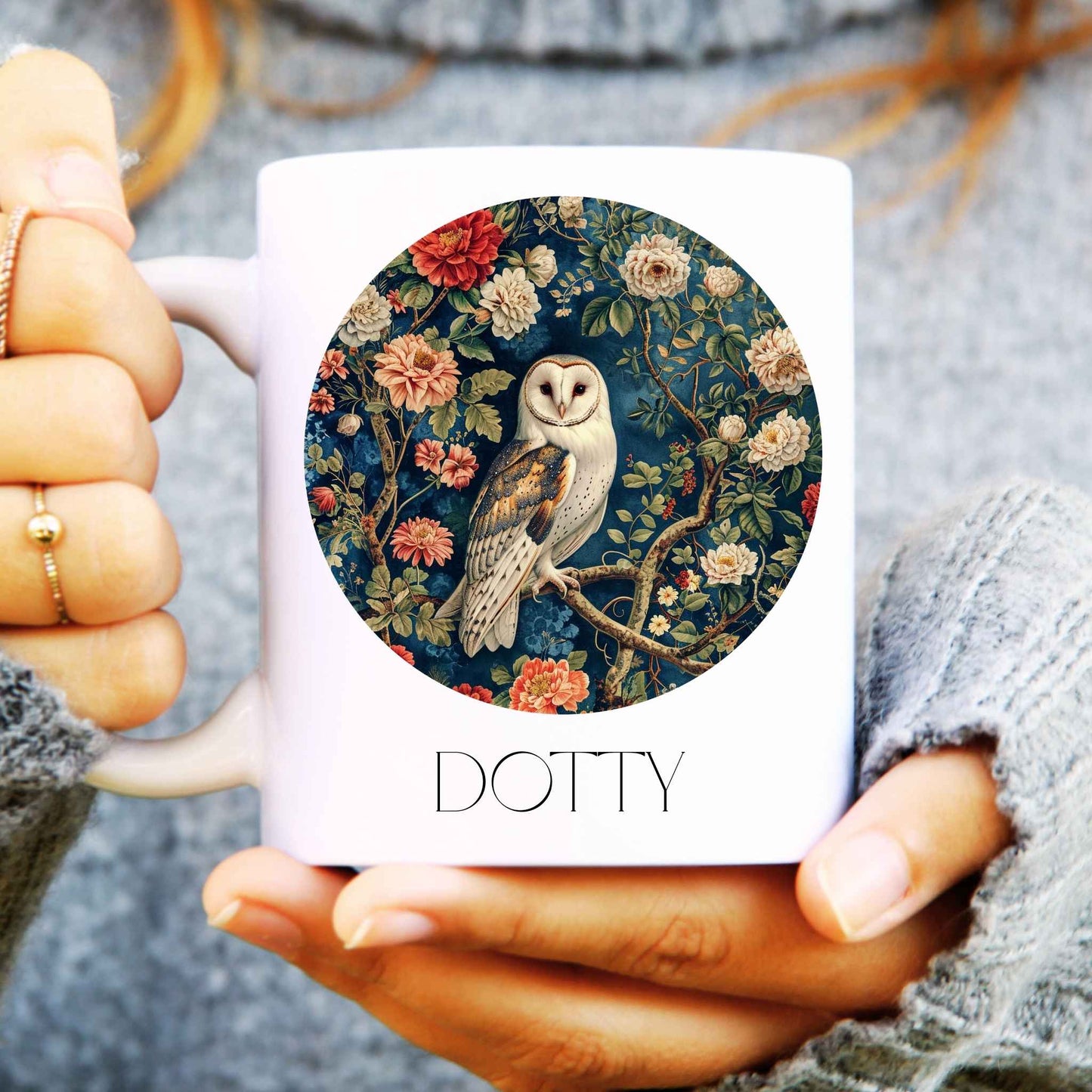 White mug with floral and owl design held by a person wearing a grey sweater.