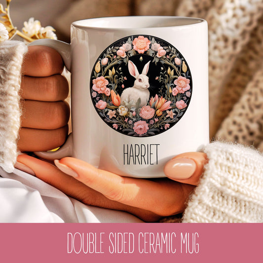 A ceramic coffee mug with a floral and animal design, featuring a rabbit, flowers, and the name 'Harriet'.