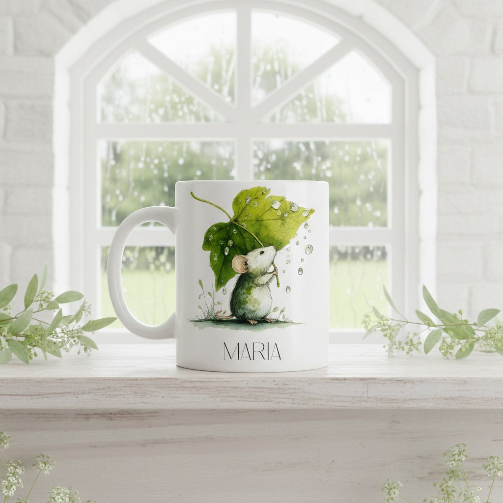 White mug with a mouse holding a leaf design on a windowsill with greenery.