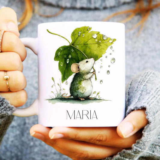 Person holding a mug with a mouse and leaf illustration and 'MARIA' text.